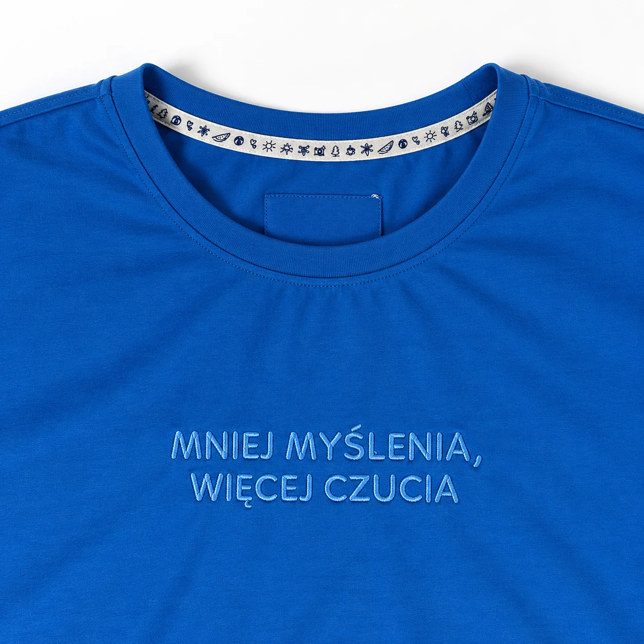 Makro haftu MNIEJ MYŚLENIA, WIĘCEJ CZUCIA na kobaltowym t-shircie